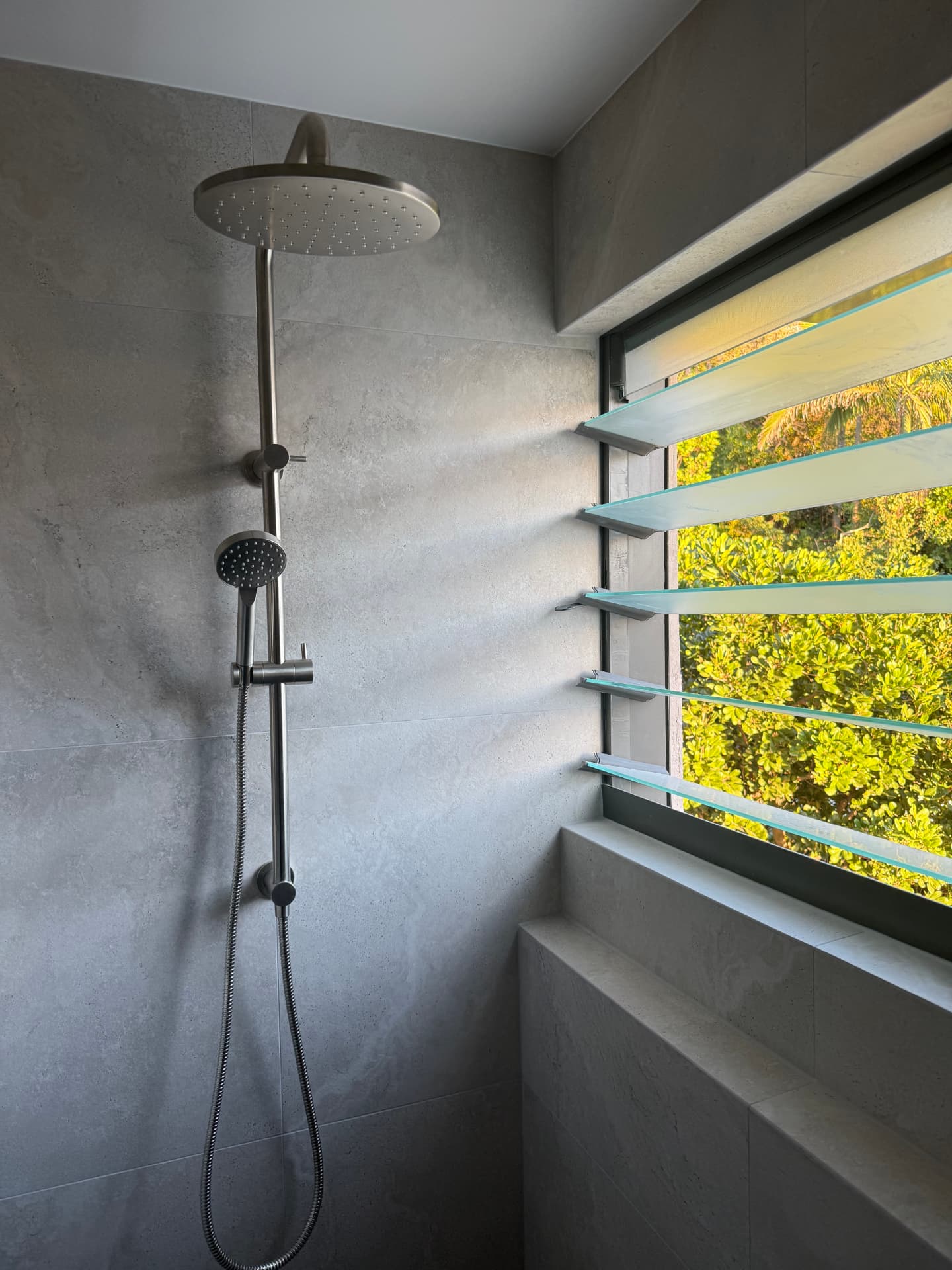 Floor-to-ceiling tiled shower wall with a rain head and louvre window